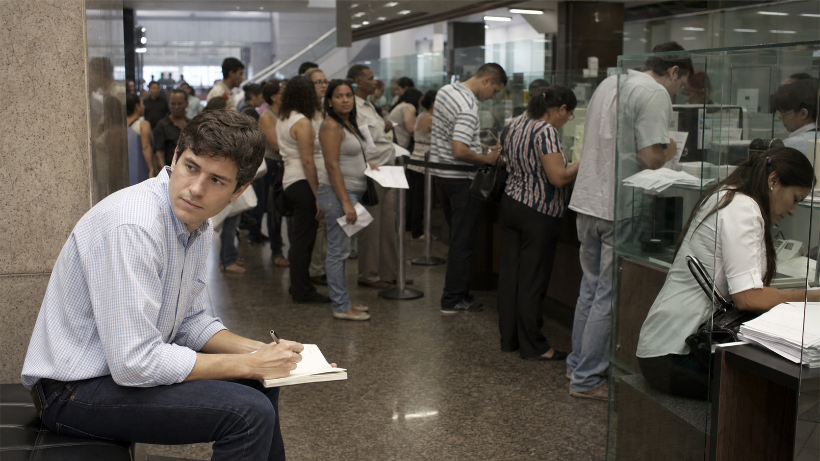 David Vélez observing the long queues and paperwork inside a traditional Brazilian bank branch